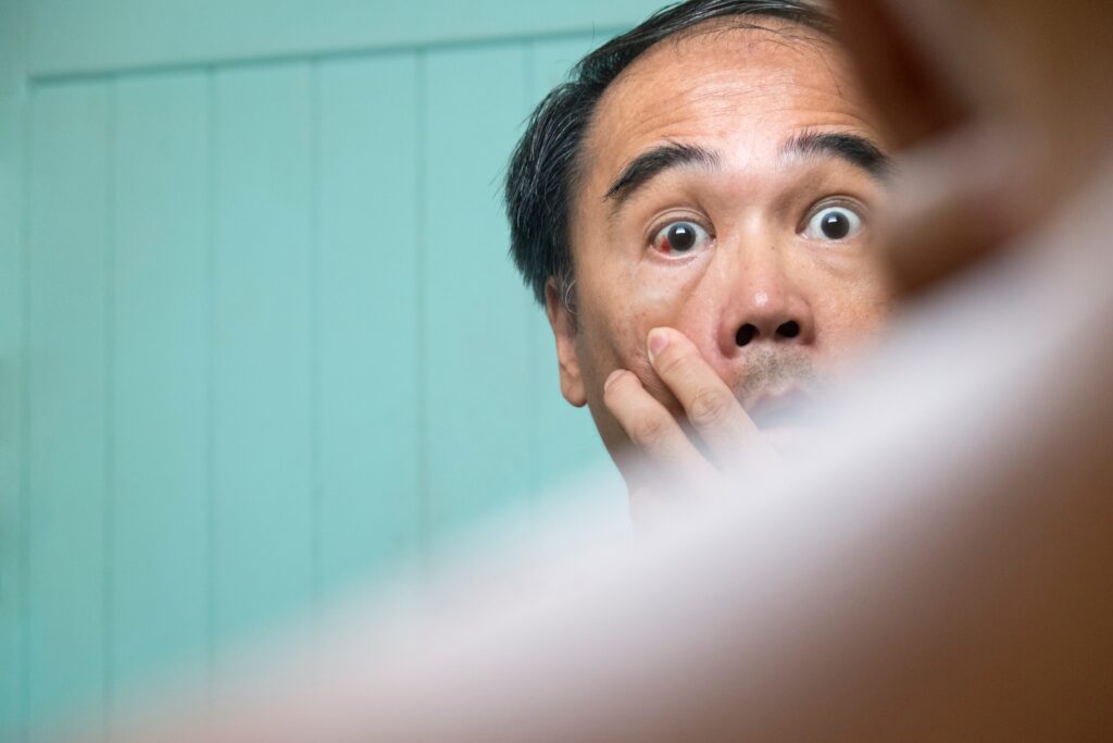 Man checking red eye in front of mirror at home - McLean Eyecare Center